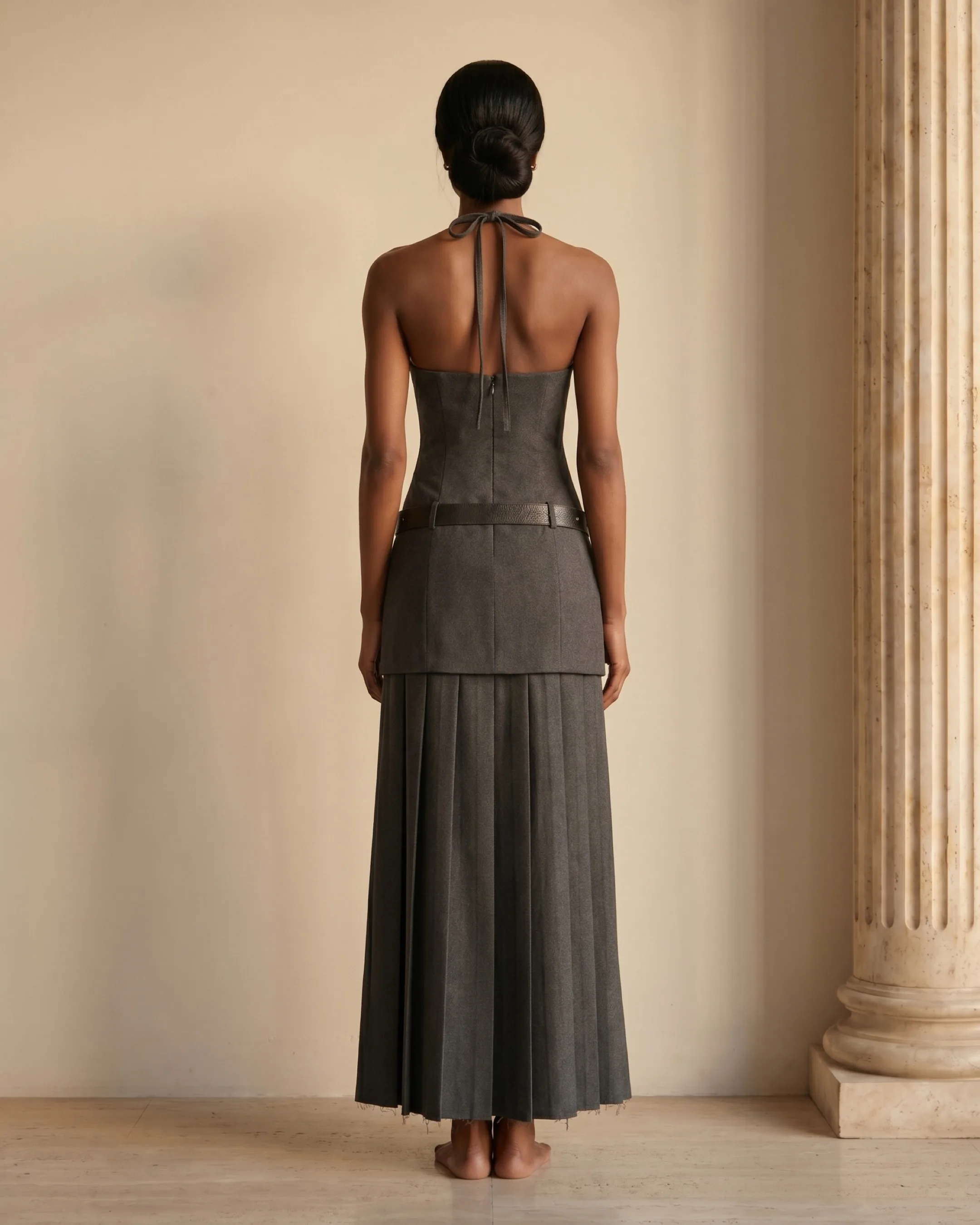Hugo Caesar Tassi Verania full-length rear view showing the open halter back, centre-back zip, studded belt and long pleated skirt