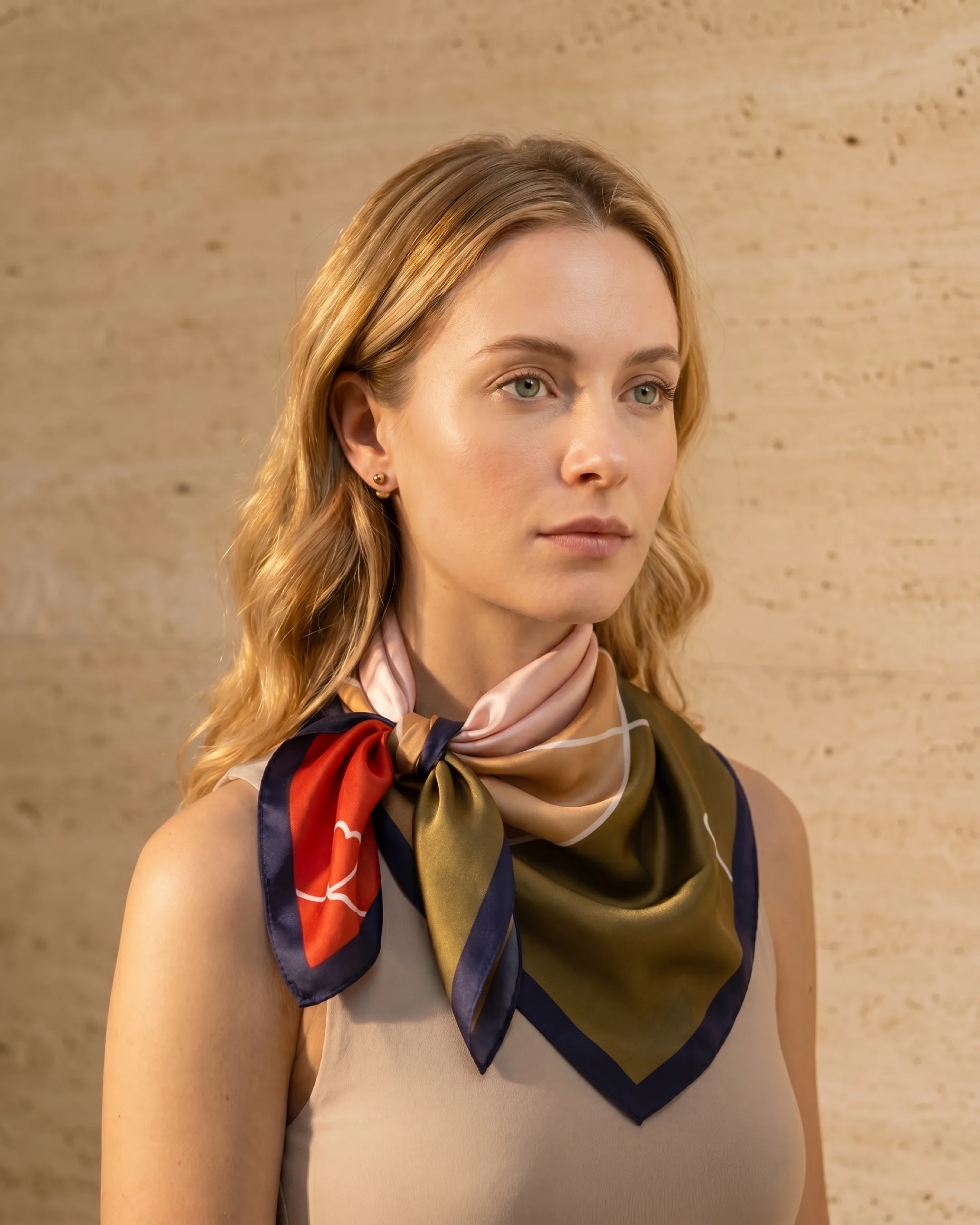 Hugo Caesar Tassi Verona silk neckerchief knotted at the throat of the model against a warm travertine wall, showing the navy border and heart motif