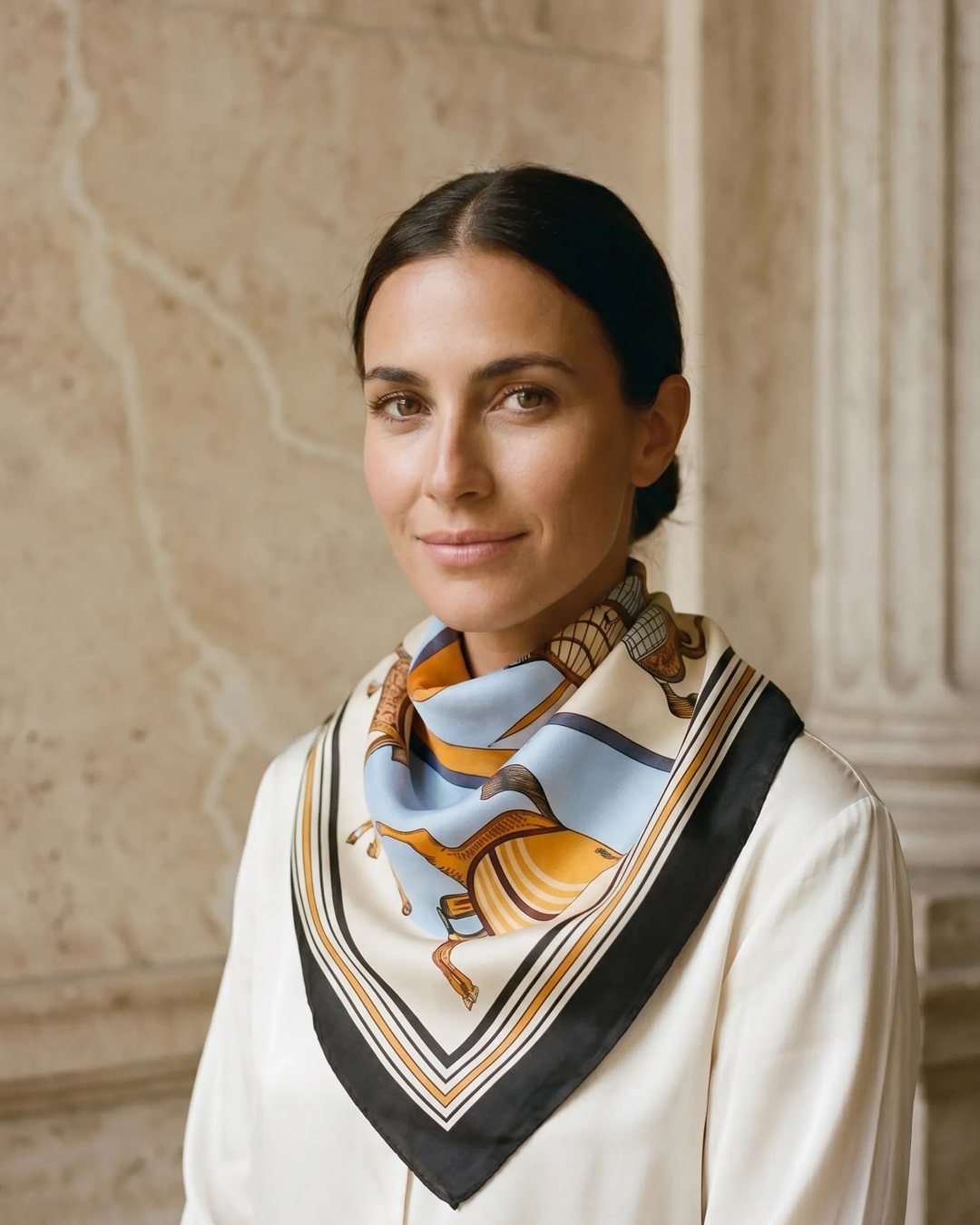 Hugo Caesar Tassi Vesta equestrian-print silk-look square scarf in Avorio, knotted at the neck of a model in a warm Roman travertine studio