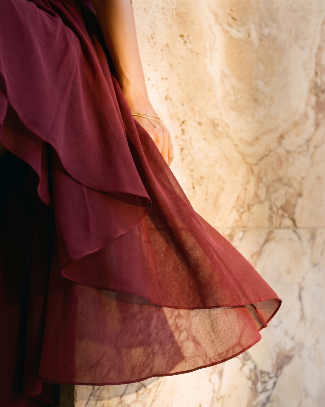 Macro detail of the Hugo Caesar Tassi Vibia dress's fluid wine-red Porpora chiffon and tiered high-low ruffle