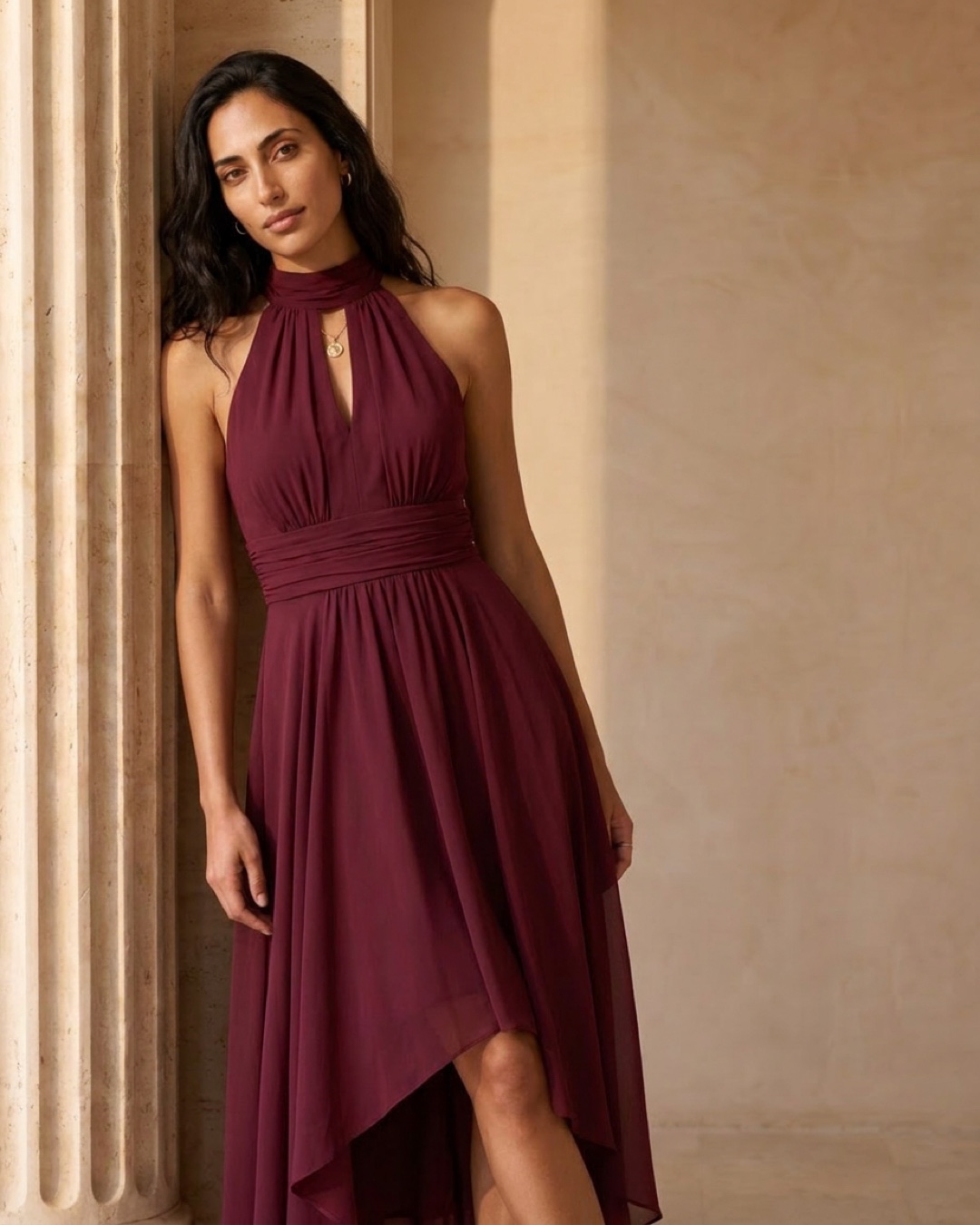 Editorial portrait of the Hugo Caesar Tassi Vibia halter-neck chiffon evening dress in Porpora among Roman travertine columns in golden light