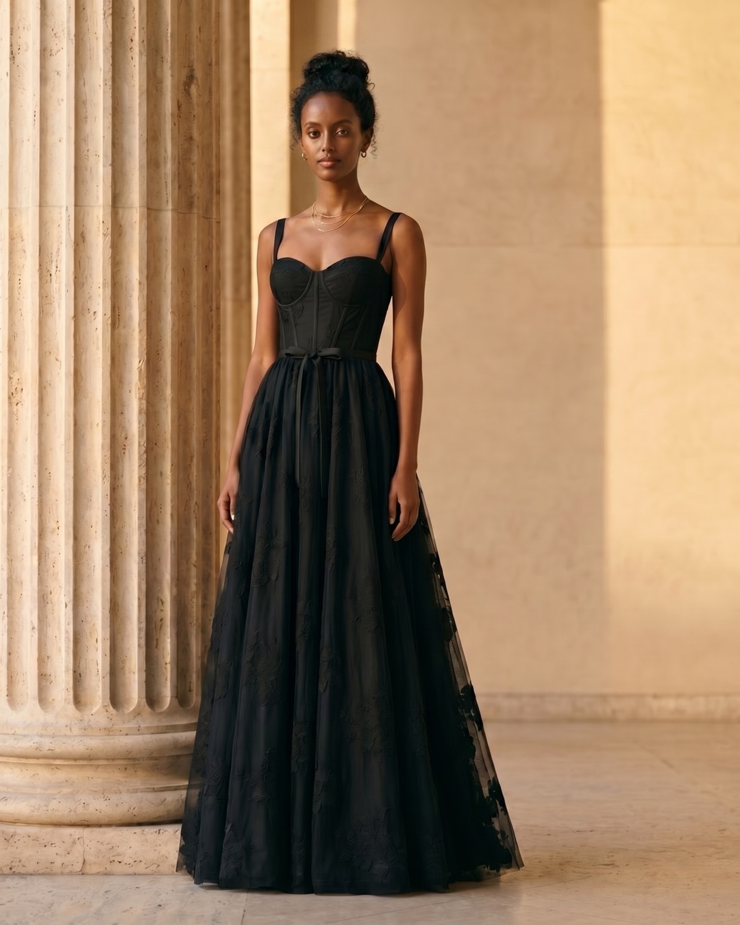 Hugo Caesar Tassi Volusia black fit-and-flare gown beside a fluted travertine column in soft golden light